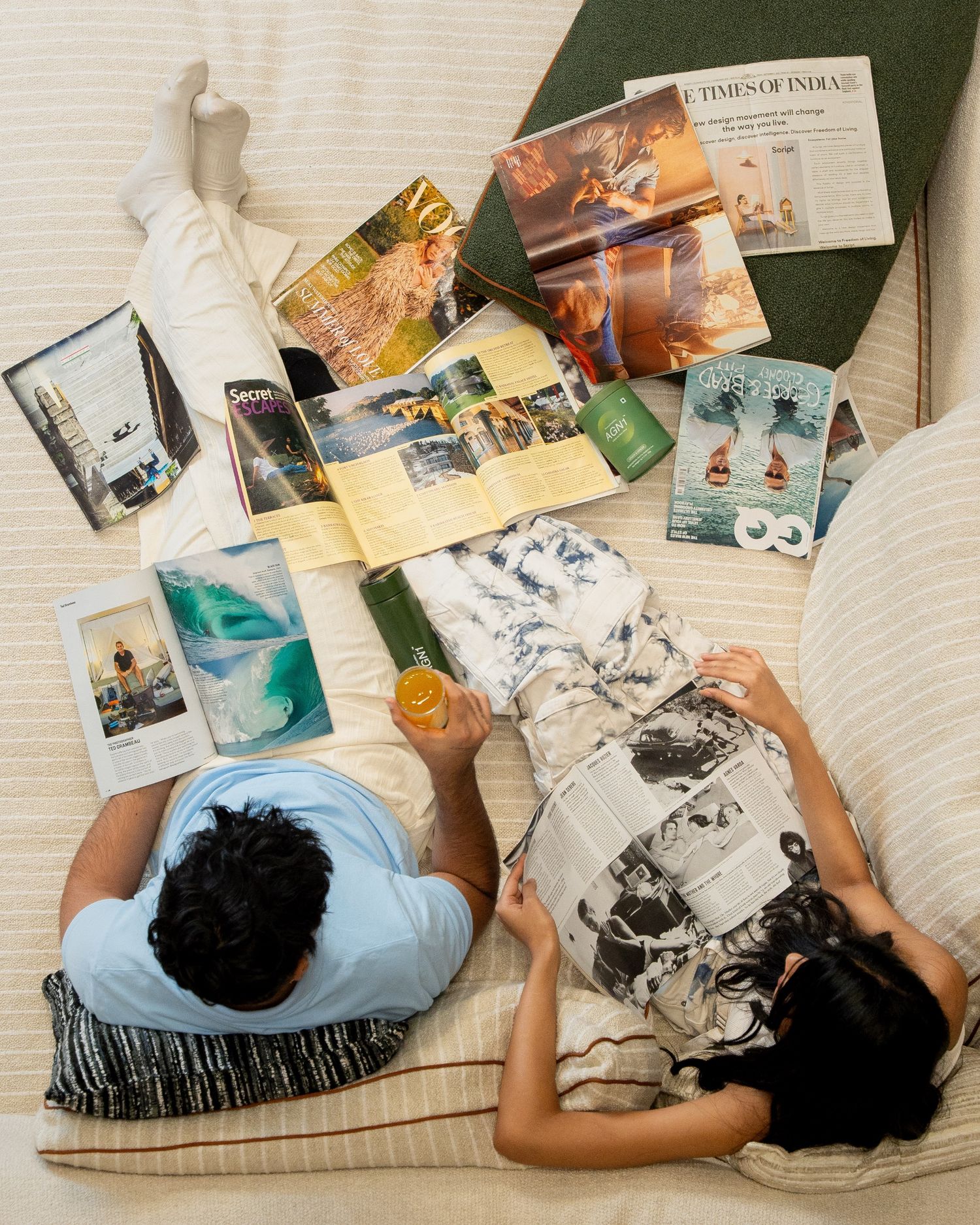 Two people reading magazines and newspapers on a cream sofa