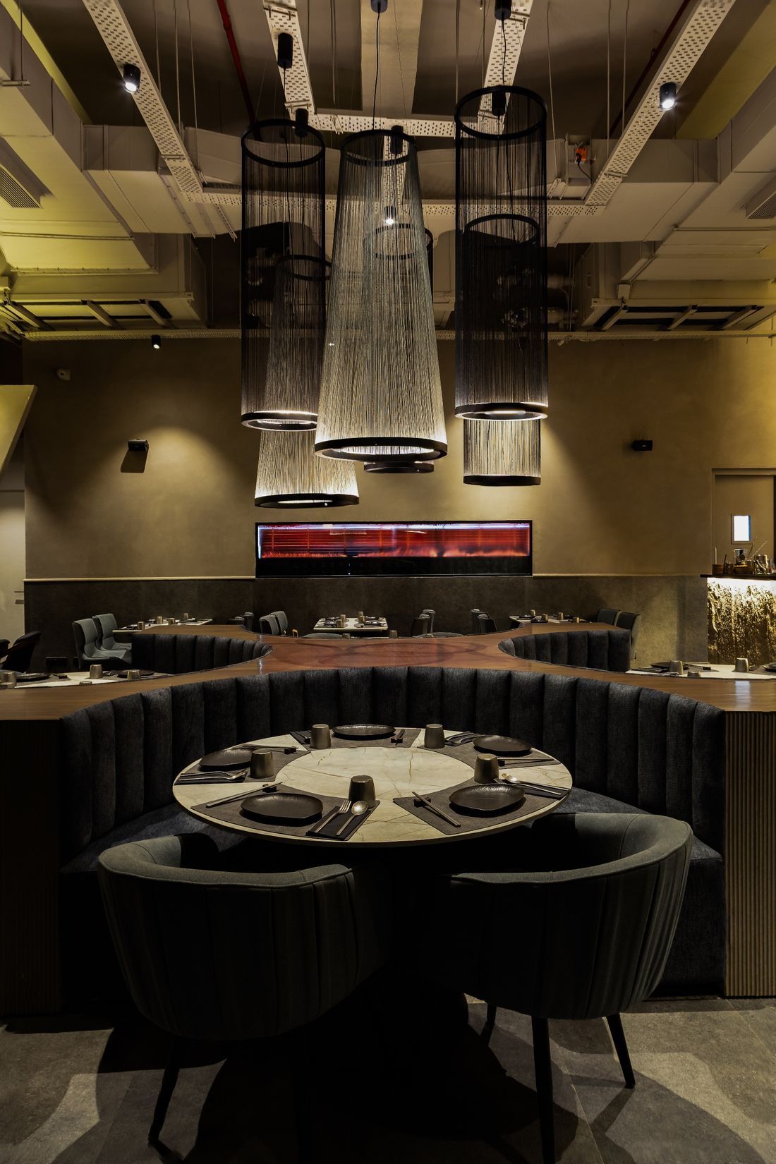 Dark restaurant interior with round booth tables beneath fibre pendant lights