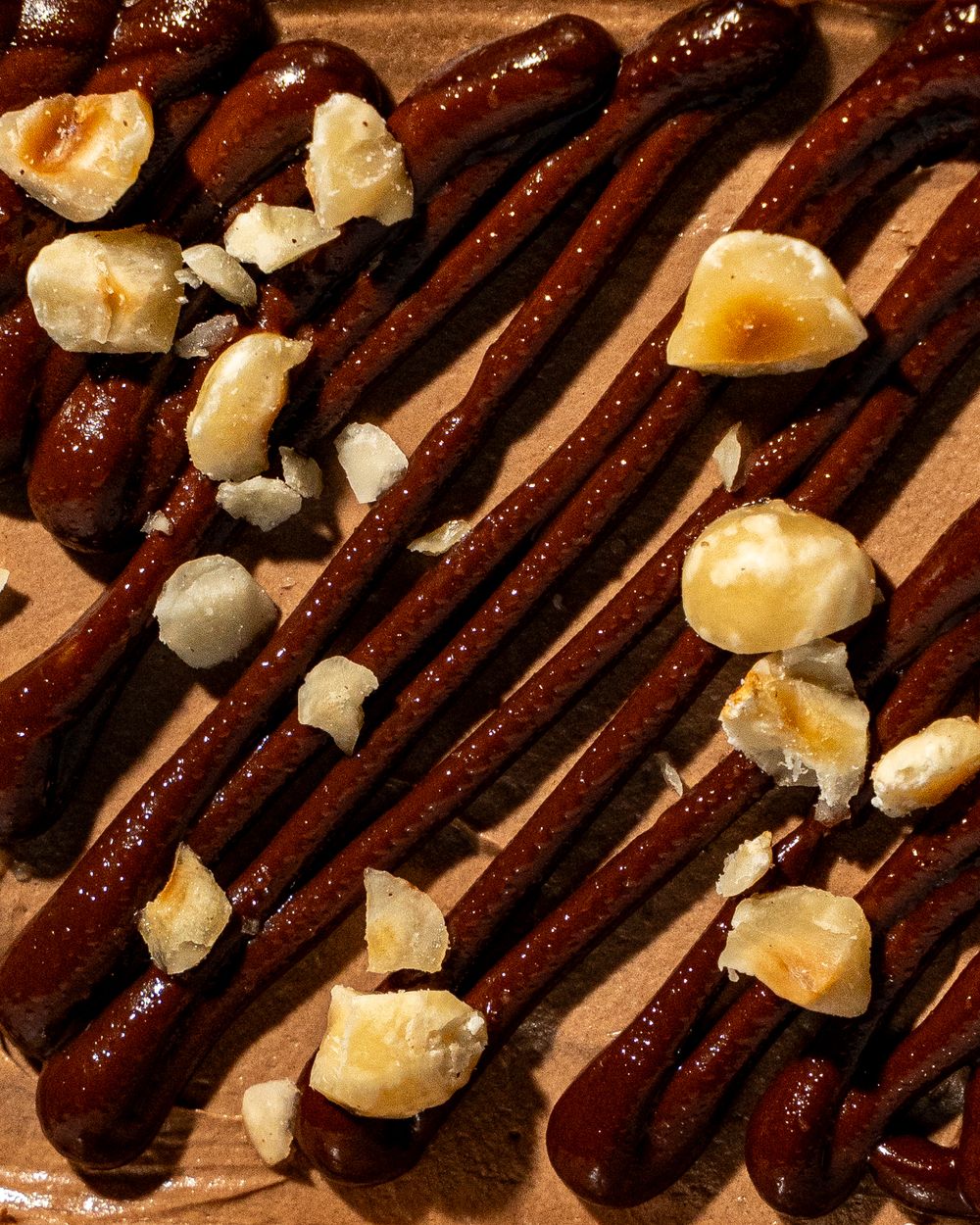 Close-up of chocolate piped over a creamy surface scattered with toasted hazelnuts