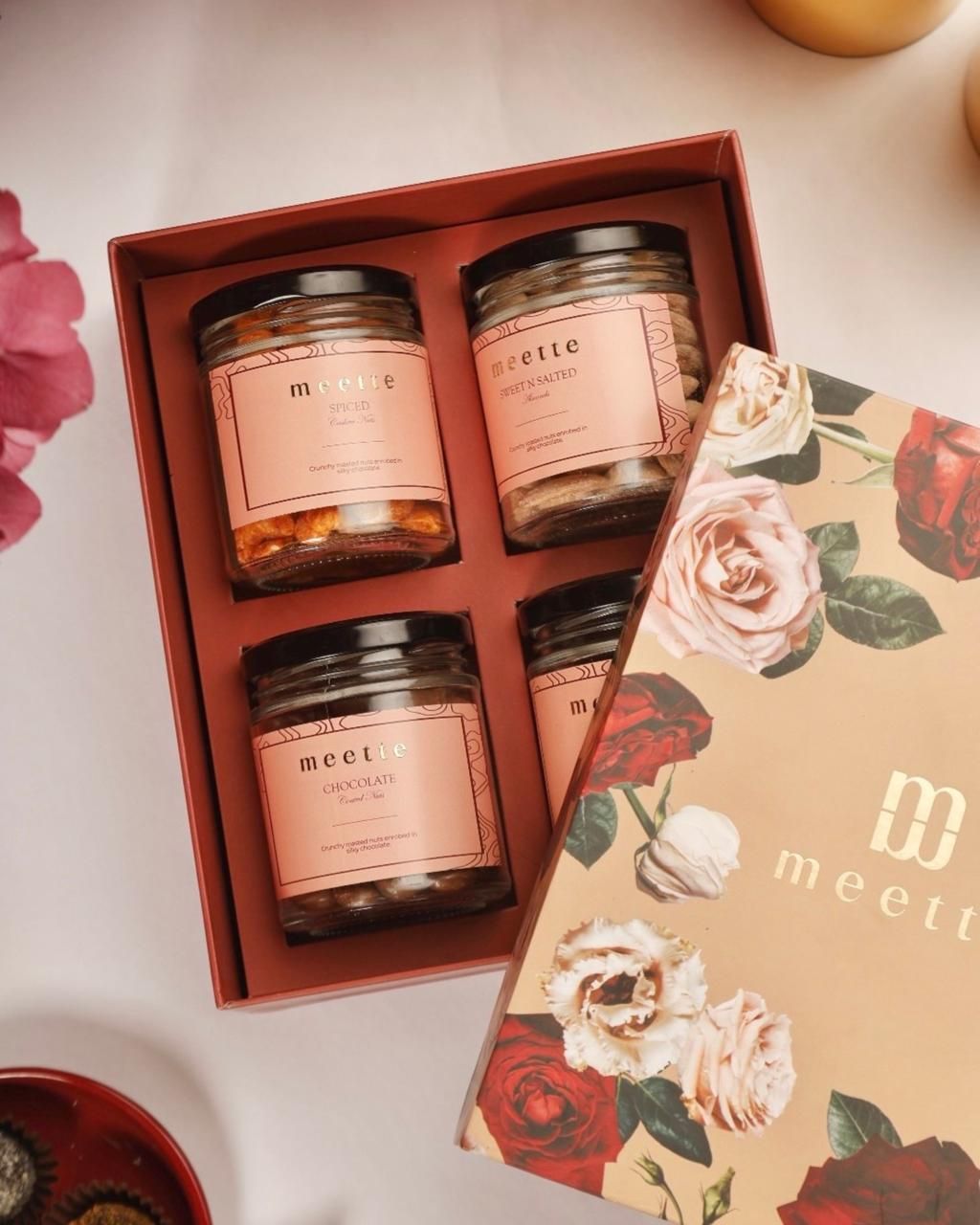 Open Meette box with four jars of chocolate-coated nuts beside a floral lid