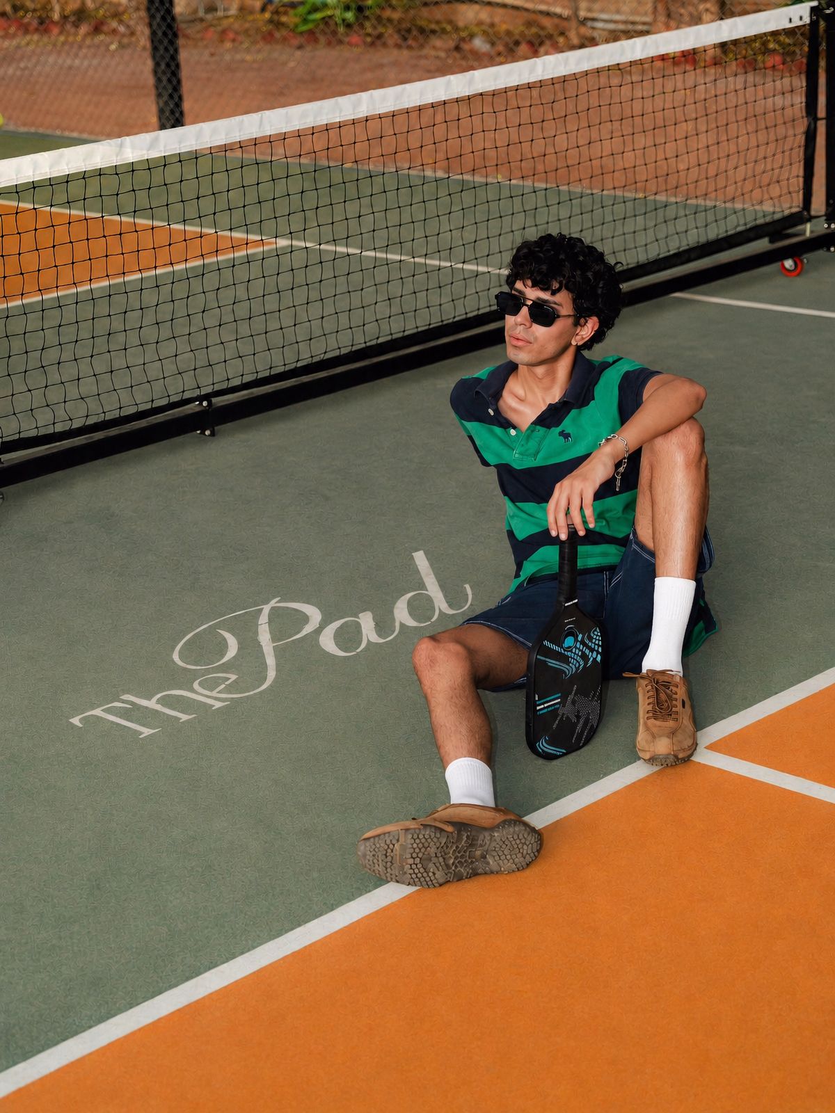 Man in a green striped polo sitting by the net beside The Pad lettering on the court